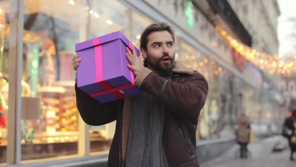 Excited man shaking with christmas present outdoors — Stockvideo