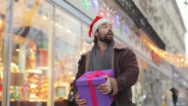 Man in santa hat with gift greeting someone on street — Stock videók