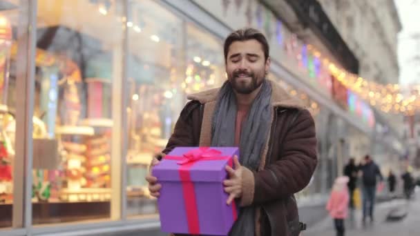 Cheerful man dancing happily on street with christmas gift — Stockvideo