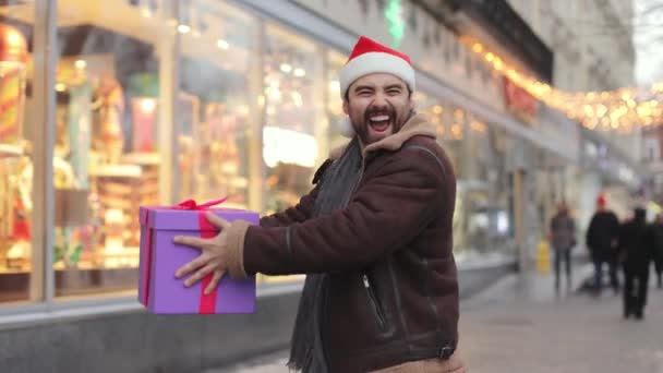 Funny man in santa hat dancing with gift box on street — Stockvideo