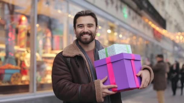 Leende man poserar nära butiken med julklappar i händerna — Stockvideo