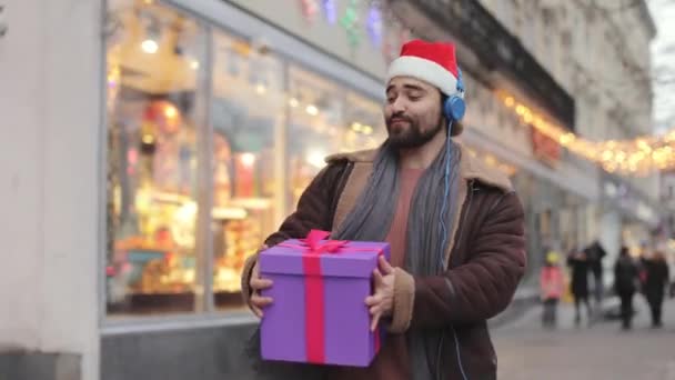 Muž ve sluchátkách tanec s vánoční dárek na ulici — Stock video