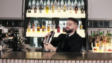 Siyah takım elbiseli ve kravatlı yakışıklı barmen özel karıştırıcı kullanarak alkolik yapıyor. Beyaz erkek barmen lüks restoranda eşsiz bir tariften kokteyl hazırlıyor..