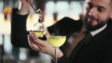 Siyah takım elbiseli yakışıklı, portakal ve biberiyeyle süslenmiş sarı alkolik içeceği sıkan adam. Profesyonel barmen iş yerinde lezzetli bir kokteyl hazırlıyor..