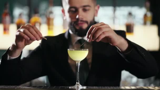 专业的酒保 身穿黑色西服 打着领带 用小衣针和薰衣草枝条精心装饰美味的酒精鸡尾酒 餐厅服务和独特菜谱的概念 — 图库视频影像