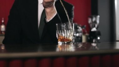 Kadehini ölçme kabından bardağa dolduran yetenekli barmene yaklaş. Siyah takım elbiseli ve kravatlı beyaz adam barın arkasında kokteyl yapıyor..