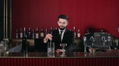 Siyah takım elbiseli olumlu bir genç tezgahın arkasında duruyor, taze alkollü kokteyl hazırlarken kaşıkla tüm malzemeleri karıştırıyor. Müşteri hizmeti, restoran ve barmen kavramı.
