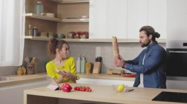 Neşeli beyaz çift evde yemek pişirirken uzun ekmekle kavga ediyor. Genç adam ve kadın mutfakta durup eğleniyorlar..