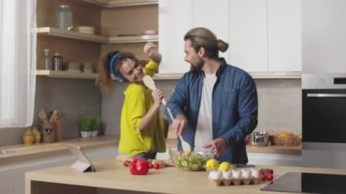 Yanında şarkı söyleyip dans eden kulaklıklı kadın varken tabakta sebze salatası hazırlayan yakışıklı beyaz adam. Mutfakta evli mutlu bir çift..