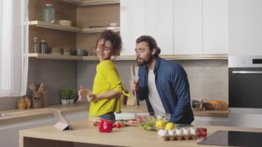 Neşeli evli çift dans ederken ve şarkı söylerken ev mutfağında yemek pişirmekten zevk alıyor. Aile zamanı, mutluluk ve aşçılık kavramı.