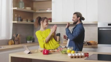 Tasasız beyaz çift, günlük giysiler içinde ev mutfağında yemek pişirirken eğleniyor ve dans ediyorlar. Genç ve sevgi dolu insanların mutlu aile hayatı..