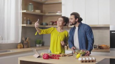 Kafkasyalı mutlu çift ev mutfağında birlikte yemek pişirirken akıllı telefondan selfie çekiyor. Genç adam ve kadın evde öğle yemeği hazırlarken eğleniyorlar..