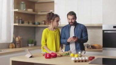 Kafkas erkek ve kadın ellerinde akıllı telefonla mutfağında yemek pişirirken yemek tarifi hakkında tartışıyorlar. İlişkiler, tartışma ve yaşam tarzları kavramı.