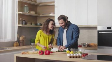 İki sevecen beyaz insan modern mutfakta yan yana duruyor taze sebzeler kesiyor, konuşuyor ve içtenlikle gülümsüyor. Aile hayatı, ilişkiler ve aşçılık kavramı.