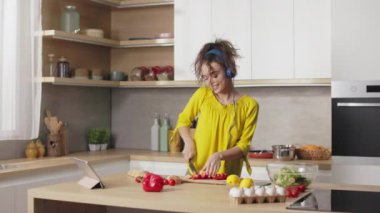 Beyaz kadın, salata için taze sebze keserken kulaklıkla müzik dinliyor. Genç bir kadın, kıvırcık kahverengi saçlı mutfakta yemek pişiriyor ve en sevdiği şarkıyı seviyor..