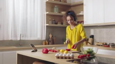 Modern kulaklıkla müzik dinleyen ve mutfakta taze sebze kesen hoş genç bir kadın. Kafkasyalı esmer modern aletlerin yardımıyla gündelik işlerden zevk alıyor..
