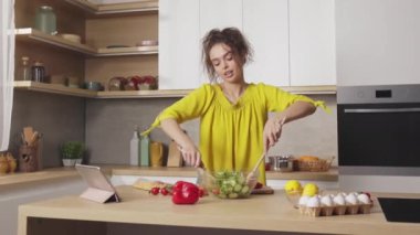 Beyaz kadın taze sebze salatasını iki tahta kaşıkla karıştırıyor. Kahverengi saçlı, ev mutfağında yemek pişirmekten hoşlanan hoş bir bayan..