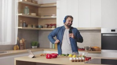 Dijital tablette müzik dinleyen ve mutfakta dans eden neşeli yakışıklı adam. Evde eğlence ve keyif dolu boş zaman..