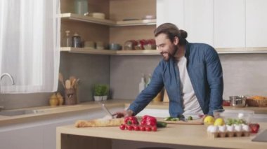 Mutfakta lezzetli yemekler hazırlarken dijital tablet kullanan gülümseyen sakallı adamın portresi. Masanın yanında taze organik sebzelerle kameraya bakan yakışıklı adam..