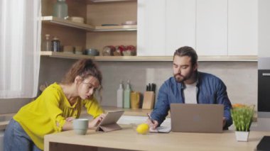 Kafkasyalı kadın ve erkek modern aletlerle mutfakta birlikte çalışıyorlar. Evde dizüstü bilgisayar, akıllı telefon ve dijital tablet kullanan evli bir çift..