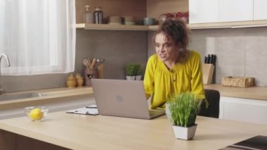 Kızgın beyaz kadın mutfak masasında otururken modern dizüstü bilgisayarda çalışıyor. Çekici esmer, zor bir görevden rahatsız olmuş. İş yerindeki sorunlar ve olumsuz duygular kavramı.