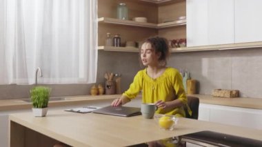 Relaxed caucasian woman closing laptop after long remote work and meditating at kitchen table. Concept of people, freelance and yoga practice.