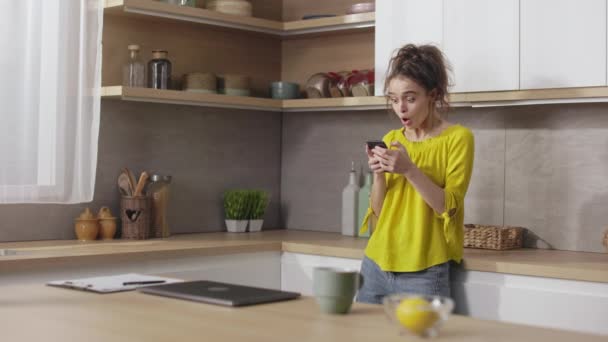 Έκπληκτη Νεαρή Γυναίκα Casual Φορούν Στέκεται Στην Κουζίνα Smartphone Στα — Αρχείο Βίντεο