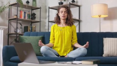 Çekici beyaz kadın, kıvırcık saçlı, nilüfer çiçekli koltukta otururken yoga yapıyor. Modern apartmandaki meditasyon sırasında parmaklarını hareket ettiren barışçıl bir kadın..