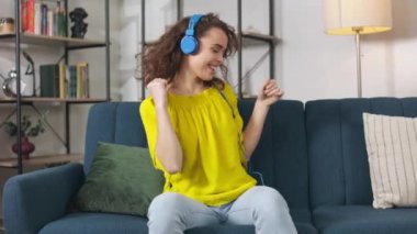 Cheerful caucasian woman in headphones sitting on sofa and listening drive song. Attractive female dancing with rhythm of music track and having fun at home.