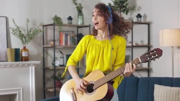 Beautiful Woman Wearing Blue Modern Headphones Playing Wooden Guitar Singing — Stock Video