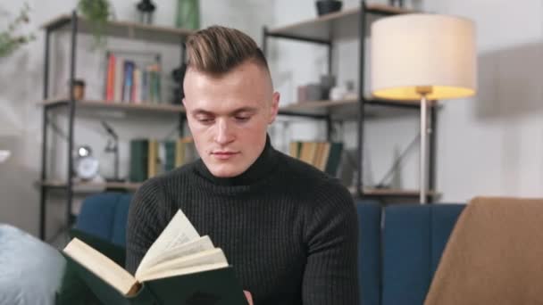 Jovem Concentrado Sentado Sofá Confortável Segurando Lendo Livro Emocionante Caucasiano — Vídeo de Stock
