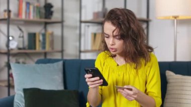 Kafkasyalı kadın elinde plastik kredi kartıyla akıllı telefon ekranına bakıyor ve para transferinde sorun yaşıyor. İnsanlar, cihazlar ve online ödeme hatası kavramı.