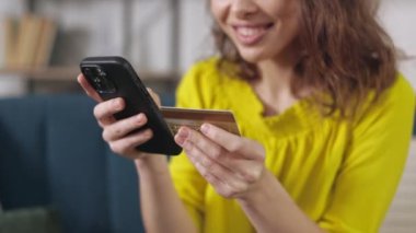 Close up of smiling young woman typing bank card number on modern smartphone for to payment during online shopping. Easy payment and gadgets concept.