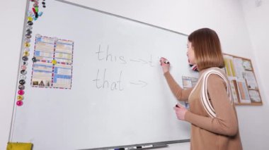 Female english tutor in casual wear writing on whiteboard grammar rules during lesson. Concept of people, education and foreingn language.