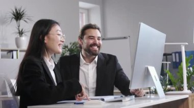 Excited diverse business partners celebrating corporate success while looking at computer monitor at modern office. Cheerful colleagues having good news and making high five gesture.