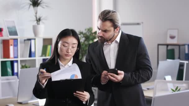 Focused Caucasian Businessman Using Mobile App While Asian Businesswoman Showing — стоковое видео