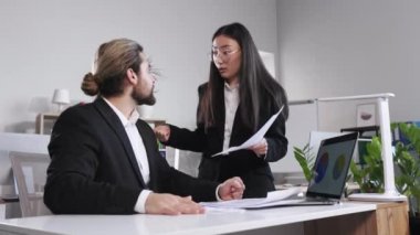 Annoyed businesswoman arguing with businessman about paperwork failure at workplace. Multiethnic colleagues having conflict over responsibility for bad work results.