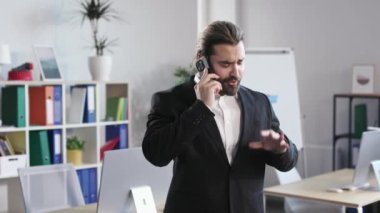 Portrait of smiling entrepreneur in formal wear making phone call with client at moden company room. Young man promising profitable terms to potential customer.