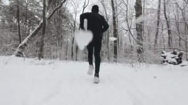 Back view of caucasian jogger in warm sportswear spending morning time at snowy forest for active cardio. Concept of people, endurance and leisure activity.