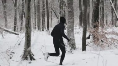 Back view of caucasian runner wearing warm sport clothes training alone among winter woodland. Healthy and active young man taking care of body by regular workout.