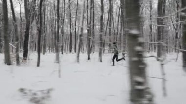 Active young runner in black sportswear enjoying regular workout on fresh air. Caucasian string man running alone at snowy winter forest. Cardio workout concept.