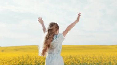 Açık havada oynarken kollarını kaldıran, doğal sarı saçlı, mutlu, beyaz bir çocuk. Arka planda mavi gökyüzü ve sarı alan.