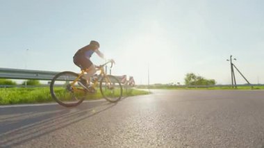 Beyaz erkek sporcu gün batımında bisiklet üzerinde sıkı çalışıyor. Genç bisikletçi her gün asfalt yolda egzersiz yapıyor..