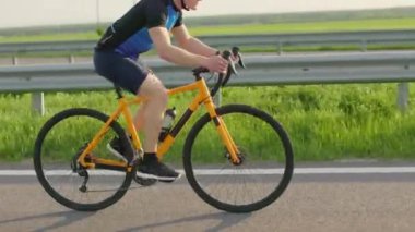 Turuncu yolda turuncu bisiklete binen aktif ve sağlıklı bir adam. Arka planda güzel bir yapısı var. Yarışma için kask ve spor kıyafeti giymiş bir erkek bisikletçi..