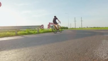 Profesyonel bisikletçi yüksek hızda yol bisikleti sürüyor ve dışarıda yoğun idmandan sonra kollarını esnetiyor. Spor anlayışı, sıkı eğitim ve sağlık faaliyetleri.