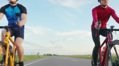 Asfalt yolda bisiklet süren iki profesyonel bisikletçi. Arka planda da güzel bir doğa var. Spor elbiseli beyaz adamlar temiz havada düzenli antrenman yapıyorlar..