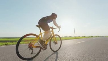 Siyah spor kıyafetli profesyonel bisikletçi ve karayolu boyunca yol bisikleti üzerinde güvenlik miğferi eğitimi. Motivasyonu, dayanıklılığı ve insanları kavrayın.