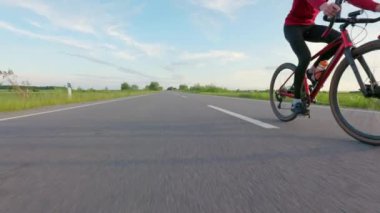 Mavi gökyüzü ve arka planda yeşil çimlerle triatlon yarışmasına hazırlanan sporcular. İki beyaz erkek karbon bisikletle ülke yolunda yarışıyor..