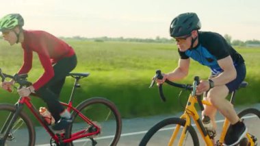 Arka planda yeşil çimlerle otoyol boyunca yüksek hızda bisiklet süren iki atlet grubu. Spor giyim rekorunu kırmaya çalışan erkekler pedal çeviriyor..