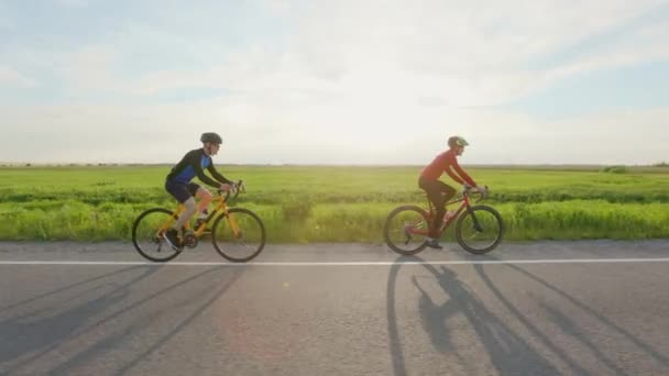 夏の日没に二人のプロアスリートが炭素自転車のトレーニングを行う 高速道路に沿って乗馬スポーツウェアやヘルメットのスポーツマン 耐久ワークアウト — ストック動画